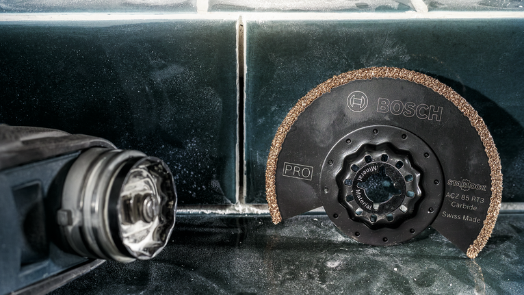 PRO ACZ 85 RT3 멀티커터 날, 85 x 2.5mm 전동 공구 옆 타일 표면에 원형 카바이드 톱날을 올려놓은 모습입니다.
