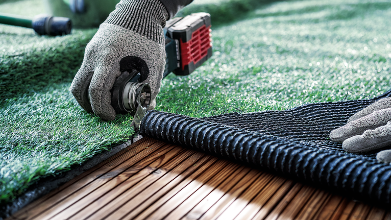 PRO ASZ 32 SC 멀티커터 날, 24 x 11mm 안전장비를 착용한 사람이 나무 데크를 따라 인공잔디를 다듬고 있습니다.