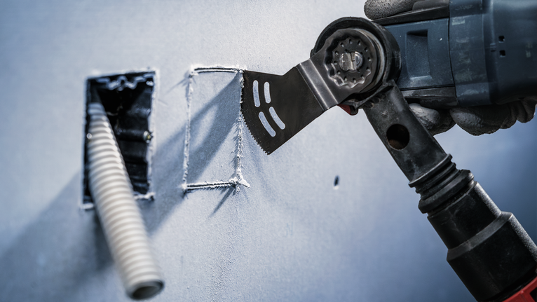 PRO AYZ 53 BPB 멀티커터 날, 53 x 40mm 안전 장비를 착용한 사람이 멀티툴을 이용해 건식벽체에 깔끔한 구멍을 뚫고 있습니다.