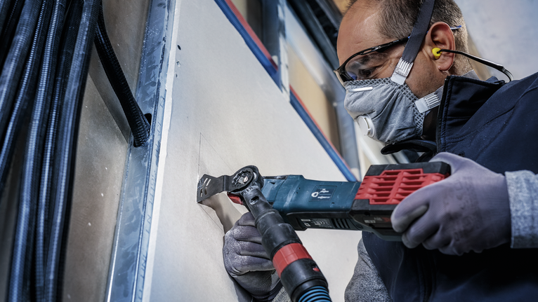 PRO AYZ 53 BPB 멀티커터 날, 53 x 40mm 안전 장비를 착용한 사람이 전동 멀티툴로 건식벽체를 자르고 있습니다.