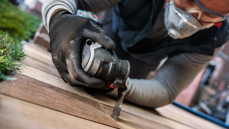 안전 장비를 착용한 사람이 전동 공구를 사용하여 나무 판자를 자르고 있습니다.