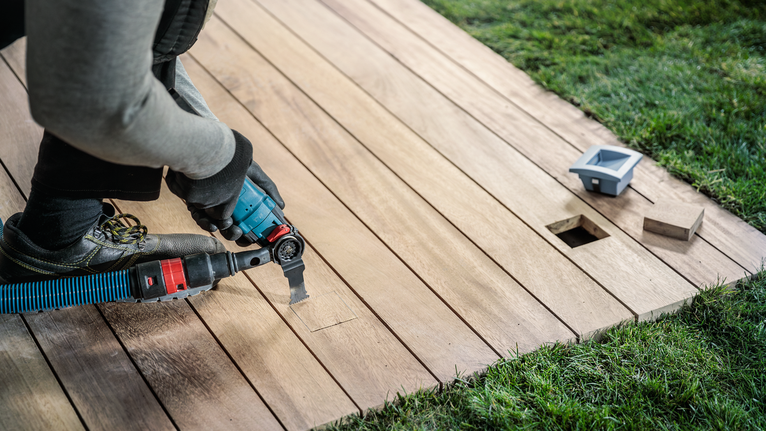 안전 장비를 착용한 사람이 전동 공구로 나무 갑판을 자르고 있습니다.