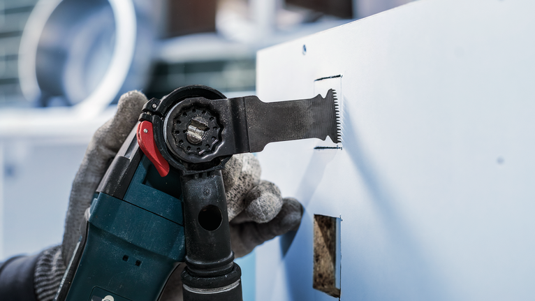 안전 장비를 착용한 사람이 전동 공구를 이용해 건식벽체에 직사각형 구멍을 뚫습니다.