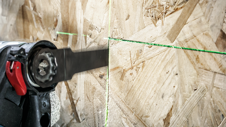 안전 장비를 착용한 사람이 왕복 운동 톱을 사용하여 녹색 가이드라인을 따라 나무를 자릅니다.