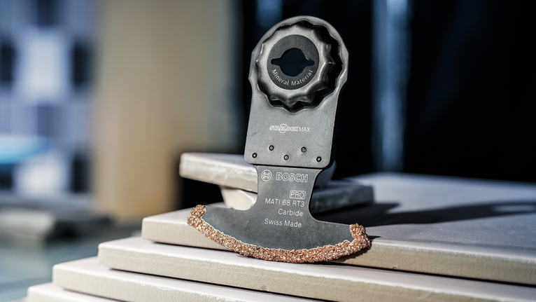 PRO MATI 68 RT3 멀티커터 날, 2.8 x 68mm 카바이드 날이 달린 진동 도구 칼날이 쌓인 세라믹 타일 위에 놓여 있습니다.