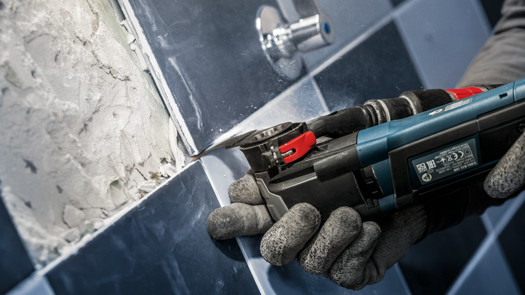PRO MATI 68 RT3 멀티커터 날, 2.8 x 68mm 안전 장비를 착용한 사람이 전동 멀티툴을 사용하여 타일에서 그라우트를 제거하고 있습니다.