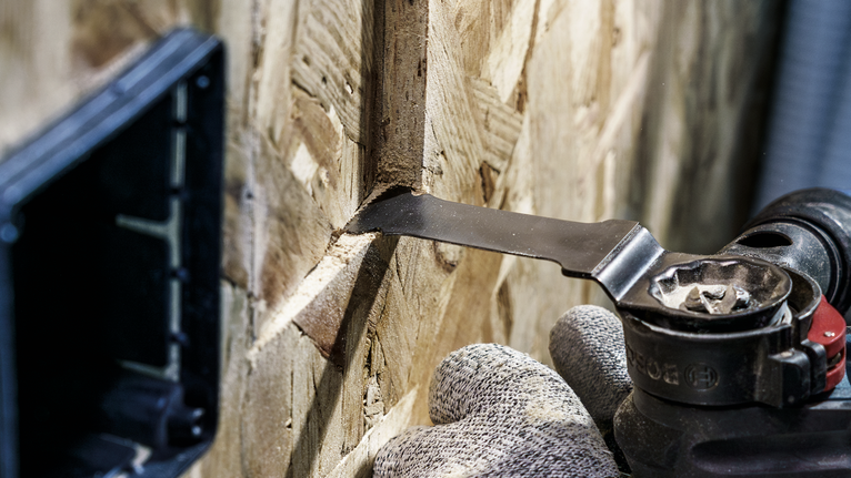 안전 장비를 착용한 사람이 멀티툴을 사용하여 목재 패널의 좁은 홈을 자르는 모습입니다.