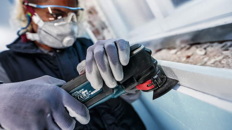 PRO ACZ 100 SWB 멀티커터 날, 100mm 안전 장비를 착용한 사람이 전동 공구로 창틀을 갈고 있습니다.