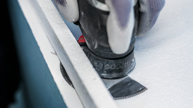 PRO ACZ 100 SWB 멀티커터 날, 100mm 안전 장비를 착용한 사람이 멀티툴 칼날로 패널 보드를 자릅니다.