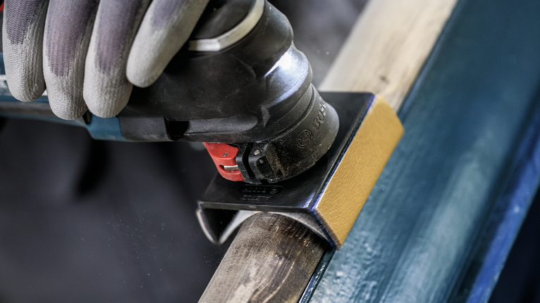 안전 장비를 착용한 사람이 전동 멀티툴로 목재를 연마하고 있습니다.