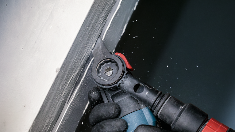 PRO MAII 32 SLC 멀티커터 날, 32 x 70mm 안전 장비를 착용한 사람이 전동 공구를 사용하여 벽 모서리 근처의 페인트를 사포질하고 있습니다.