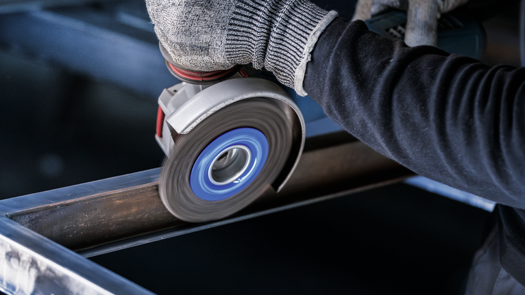 안전 장비를 착용한 사람이 각도 분쇄기를 사용하여 강철 빔을 갈고 있습니다.