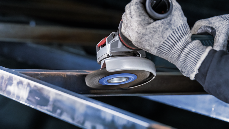 안전 장비를 착용한 사람이 각도 그라인더로 금속 빔을 연마하고 있습니다.