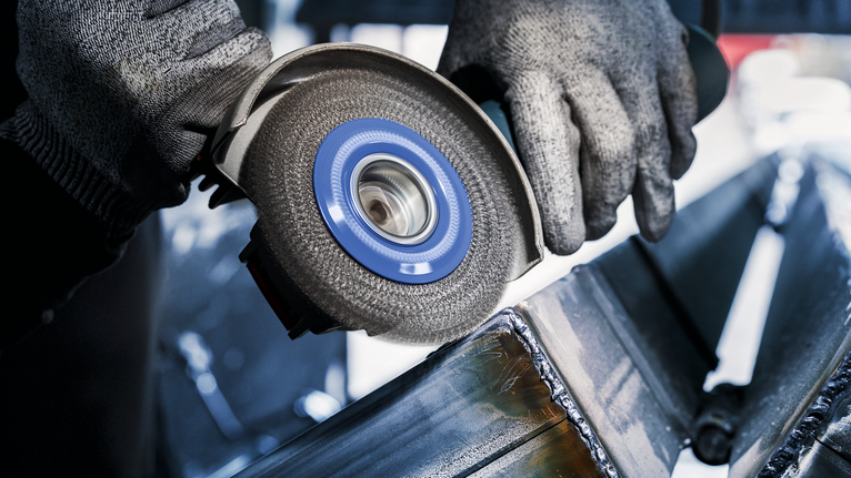 안전 장비를 착용한 사람이 각도 분쇄기로 금속 빔을 갈고 있습니다.