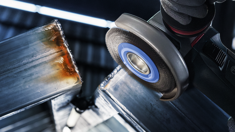 안전 장비를 착용한 사람이 각도 분쇄기를 사용하여 금속 빔을 갈고 있습니다.