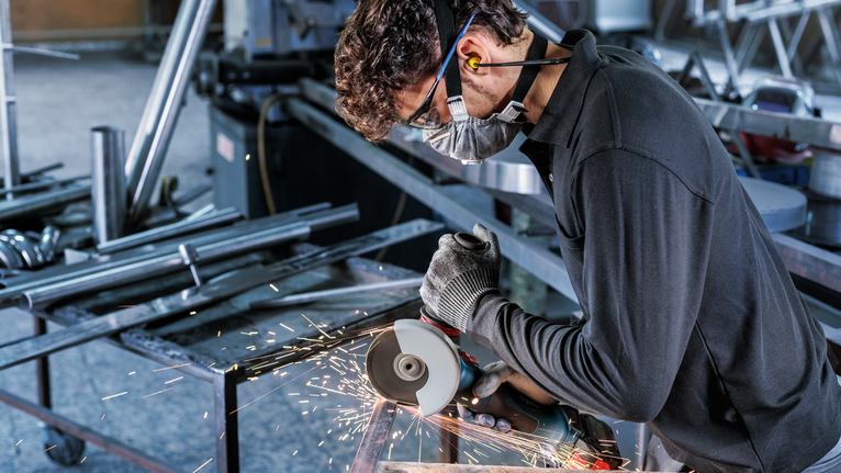 안전 장비를 착용한 사람이 각도 분쇄기를 사용하여 금속을 절단하면서 불꽃이 발생합니다.