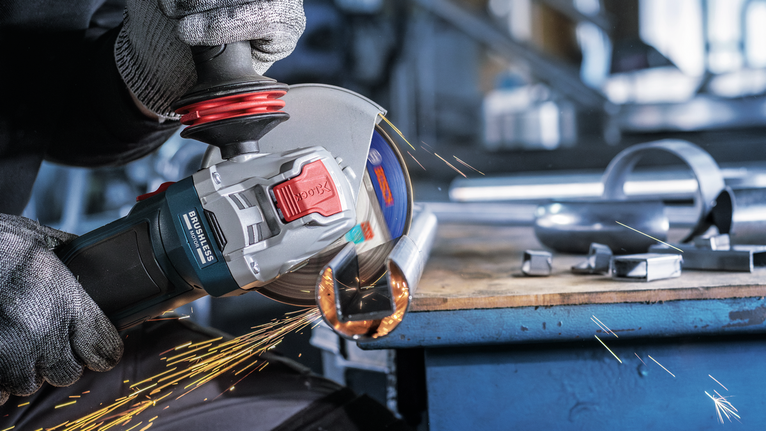 안전 장비를 착용한 사람이 금속 파이프를 갈아서 불꽃이 난다.