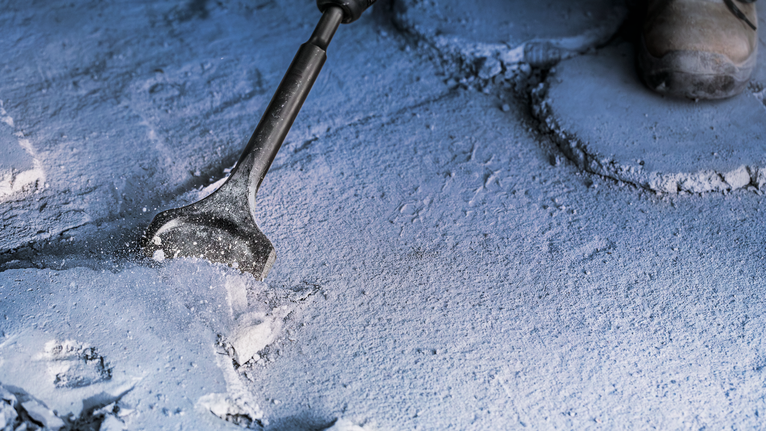 안전장비를 착용한 사람이 콘크리트 표면을 끌로 깎고 있습니다.