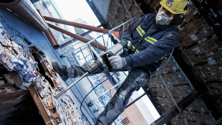 PRO SDS max-5C 포인트 치즐 400mm 안전장비를 착용한 사람이 회전 망치를 사용해 콘크리트를 깨고 있습니다.