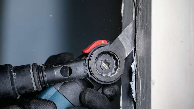 안전 장비를 착용한 사람이 전동 공구를 사용하여 벽 근처의 재료를 절단하고 있습니다.