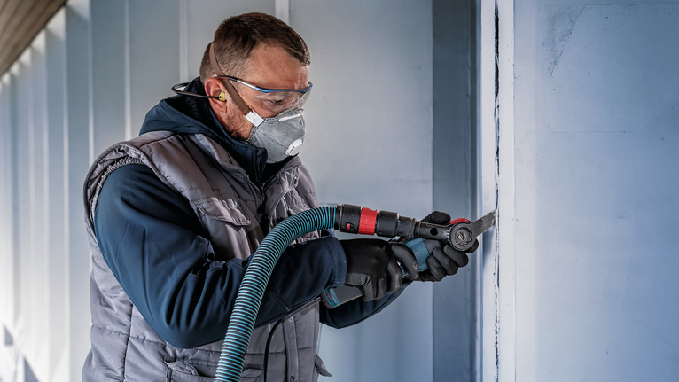 PRO MAII 32 SC 멀티커터 날, 32 x 55mm 안전 장비를 착용한 사람이 전동 공구를 사용하여 벽에 수직 홈을 만들고 있습니다.