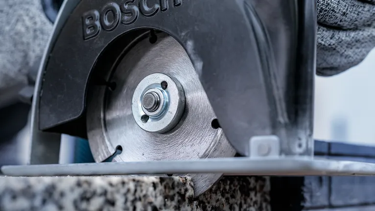 안전 장비를 착용한 사람이 원형 톱으로 돌을 자르고 있습니다.