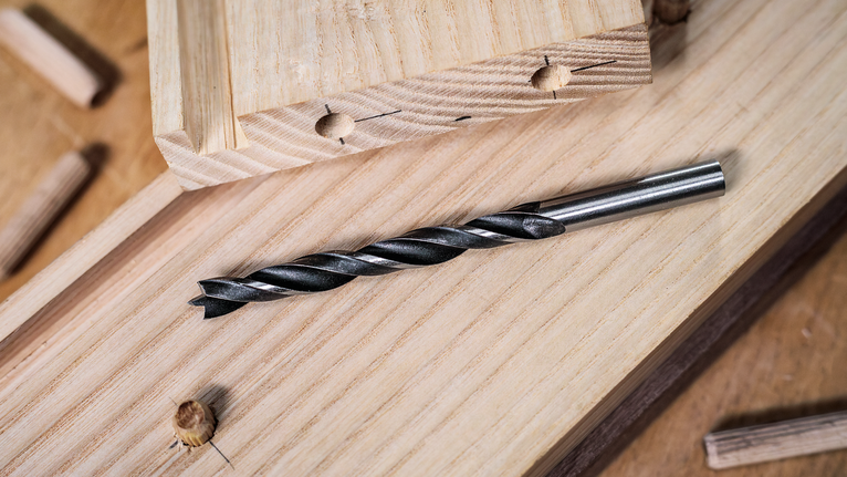 나무 판자 위에 드릴 비트를 놓고 그 근처에 막대를 꽂습니다.