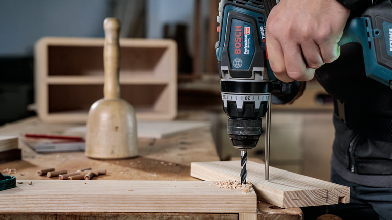 나무판에 구멍을 뚫기 위해 전동 드릴을 사용하는 사람.