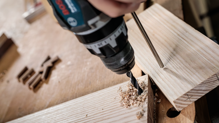 작업대 위의 나무 판자에 구멍을 뚫는 사람.