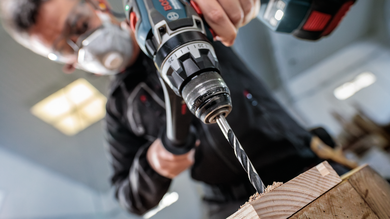 안전장비를 착용한 사람이 나무판에 구멍을 뚫고 있습니다.