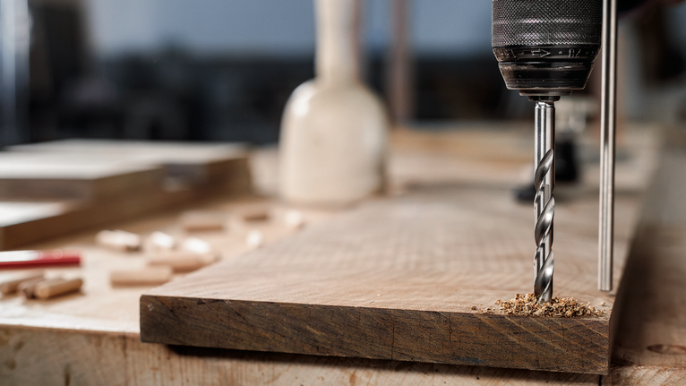 작업대 위의 나무판에 전동 드릴로 구멍을 뚫고 있습니다.