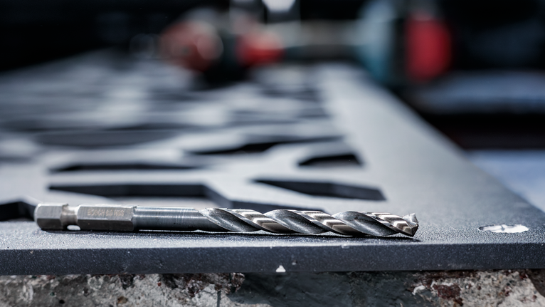 산업 작업 공간에서 금속 드릴 비트가 잘린 강철판 위에 놓여 있습니다.