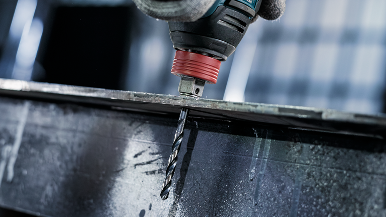 안전 장비를 착용한 사람이 금속 빔에 구멍을 뚫고 있습니다.