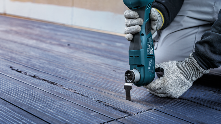 안전 장비를 착용한 사람이 전동 공구를 사용하여 나무 바닥에 홈을 파고 있습니다.