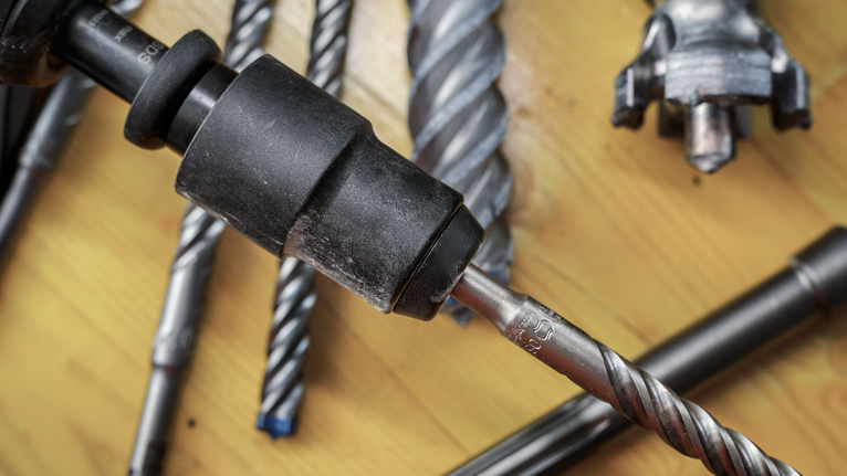 나무 표면 위에 있는 다양한 금속 드릴 비트와 드릴 척의 클로즈업.