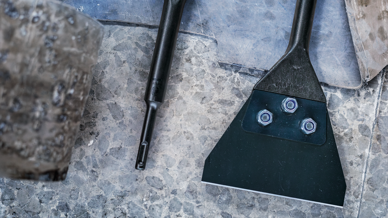 질감이 있는 돌 표면에 볼트가 달린 넓은 금속 끌입니다.