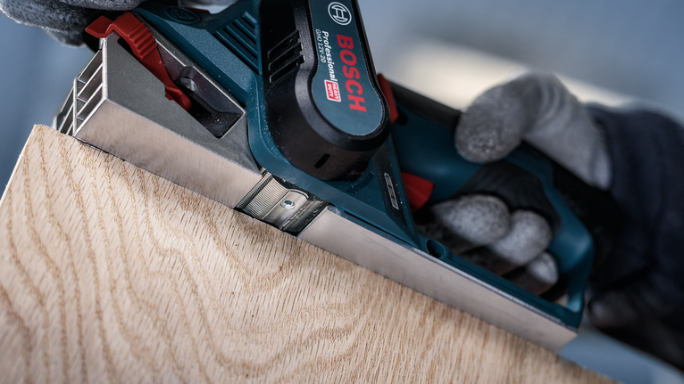 안전장비를 착용한 사람이 나무판의 가장자리를 다듬고 있습니다.