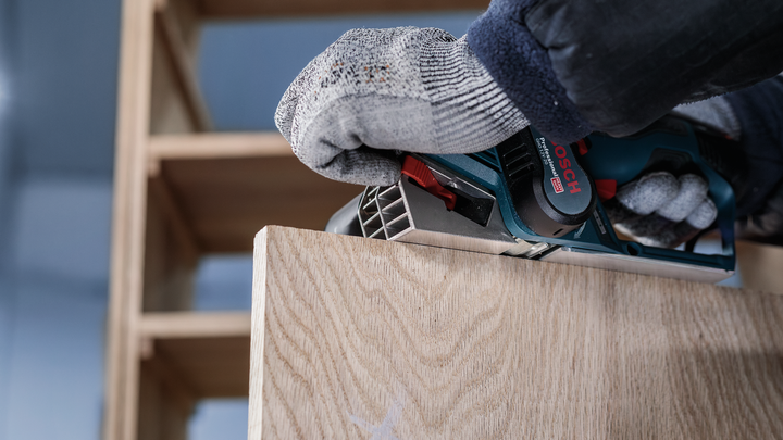 안전 장비를 착용한 사람이 나무판 위에서 전동 剪剪기를 사용하고 있습니다.