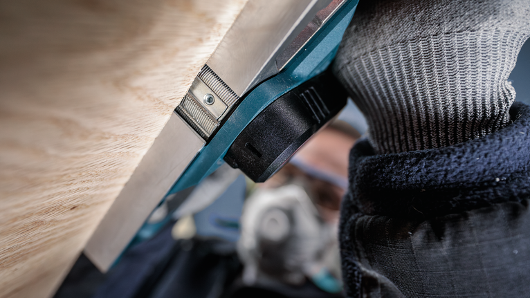 안전 장비를 착용한 사람이 나무 표면 가까이에서 전동 공구를 조작하고 있습니다.