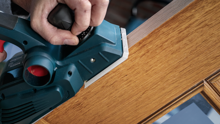 전동 刨制로 나무 문의 가장자리를 매끄럽게 다듬는 중입니다.