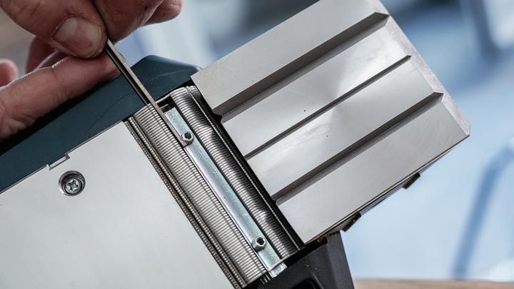 사람이 도구를 사용하여 금속 刨刻 칼날을 조정하고 있습니다.