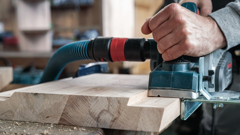 한 사람이 작업장에서 나무판 위에 전동 평면기를 사용하고 있습니다.