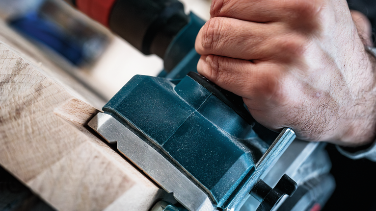 사람이 전동공구를 사용하여 나무 모양을 만듭니다.