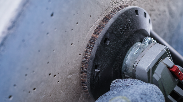 안전 장비를 착용한 작업자가 전동 공구를 이용해 콘크리트 표면을 갈고 있습니다.