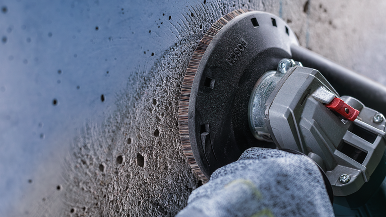 안전 장비를 착용한 사람이 각도 그라인더를 사용하여 콘크리트 벽을 매끄럽게 다듬습니다.