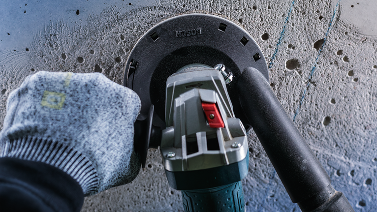 안전 장비를 착용한 작업자가 전동 공구로 콘크리트 벽을 갈고 있습니다.