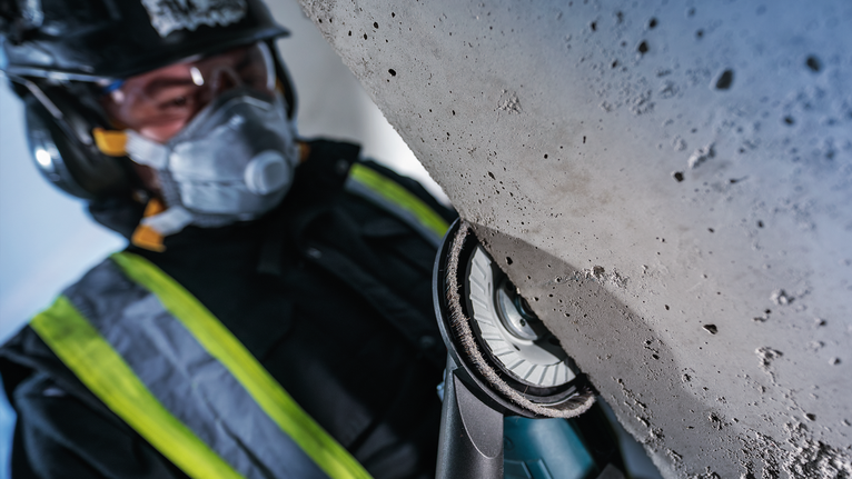 안전장비를 착용한 사람이 전동공구를 이용해 콘크리트 표면을 갈고 있습니다.