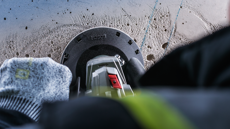 안전 장비를 착용한 작업자가 전동 공구로 콘크리트에 구멍을 뚫고 있습니다.