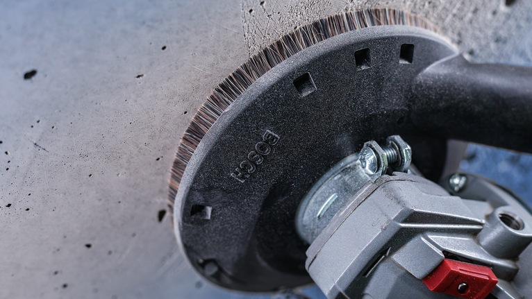 전동 공구에 부착된 와이어 컵 브러시로 콘크리트 벽의 표면을 청소합니다.