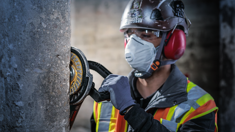 안전장비를 착용한 사람이 전동공구를 이용해 콘크리트 기둥을 갈아내고 있습니다.
